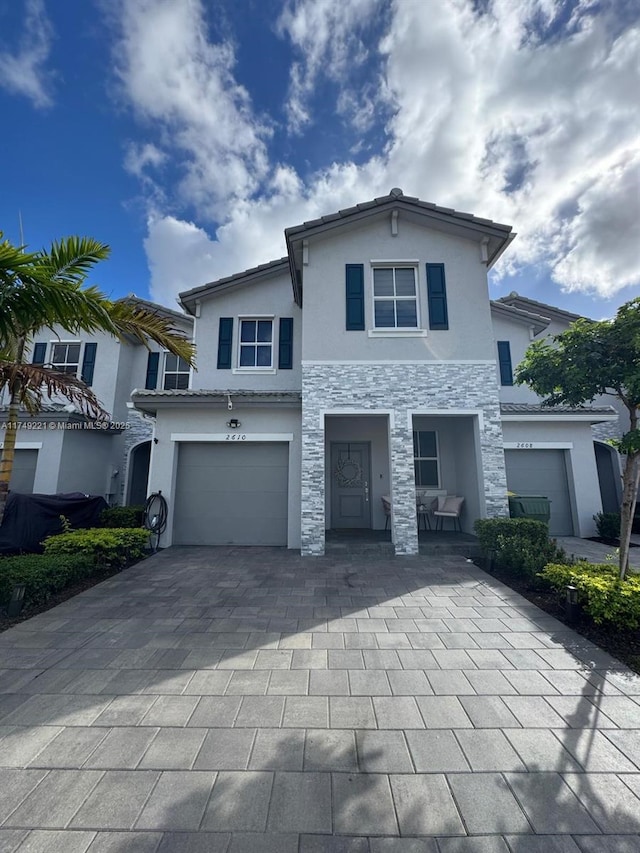 view of front of home with stone siding, decorative driveway, an attached garage, and stucco siding