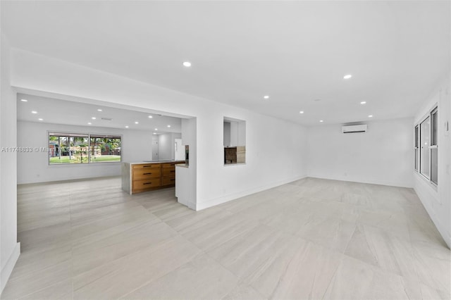 unfurnished living room with baseboards, an AC wall unit, and recessed lighting