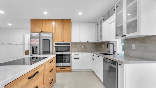 kitchen with appliances with stainless steel finishes, a sink, glass insert cabinets, and white cabinets