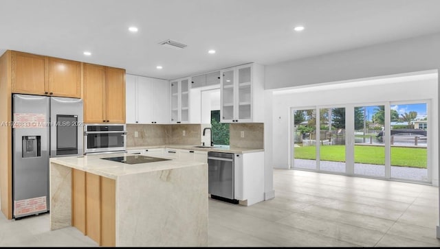 kitchen with a kitchen island, white cabinets, appliances with stainless steel finishes, tasteful backsplash, and glass insert cabinets