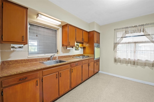 kitchen featuring gas stovetop, a sink, baseboards, light countertops, and brown cabinets