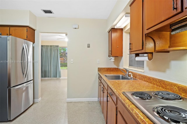 kitchen with a sink, visible vents, freestanding refrigerator, stovetop, and brown cabinetry