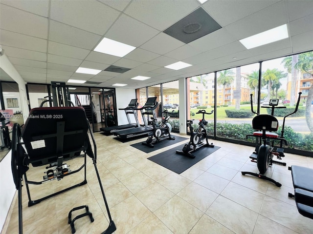 workout area featuring a paneled ceiling, floor to ceiling windows, and light tile patterned floors