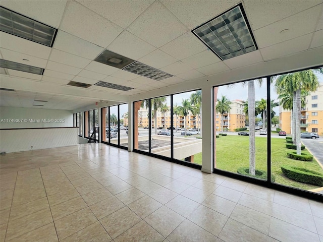 empty room with a wealth of natural light, visible vents, a paneled ceiling, and light tile patterned flooring