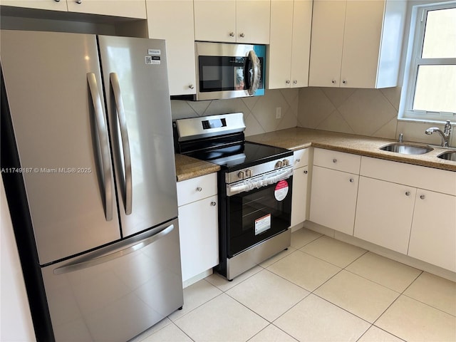 kitchen with light tile patterned floors, stainless steel appliances, backsplash, white cabinetry, and a sink