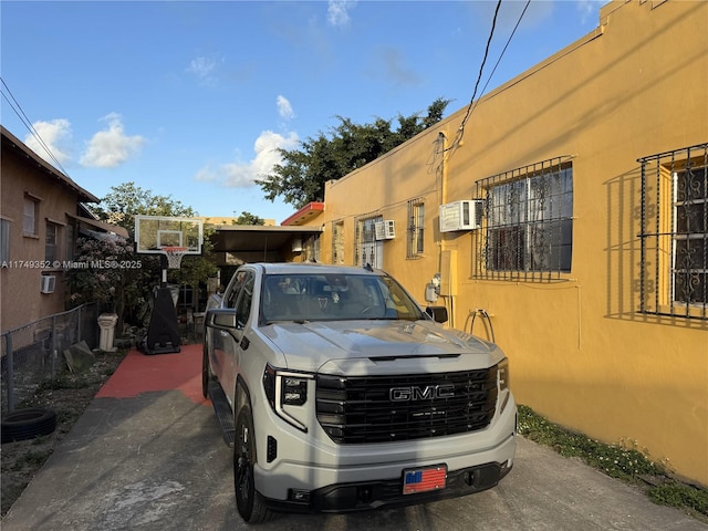 view of car parking featuring fence and a wall mounted AC