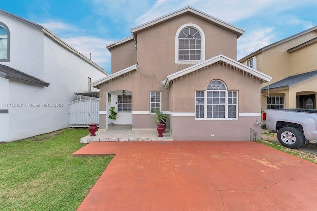 rear view of property featuring a gate, a yard, and stucco siding