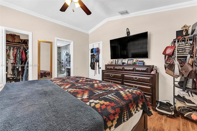 bedroom featuring a walk in closet, visible vents, ornamental molding, vaulted ceiling, and wood finished floors