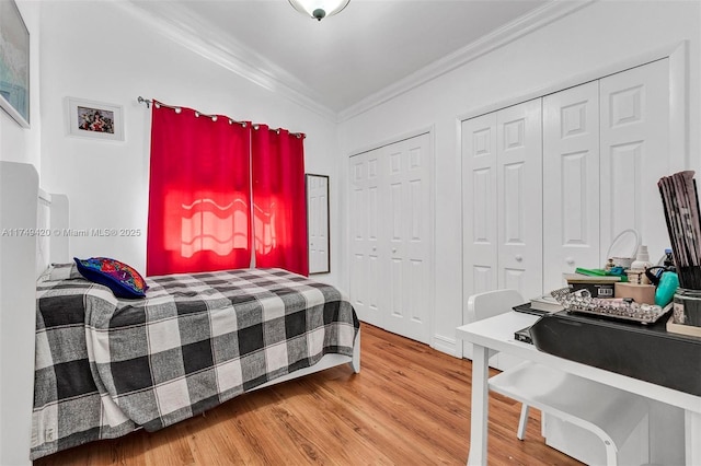 bedroom with two closets, crown molding, and wood finished floors