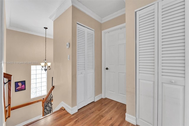 corridor with light wood finished floors, baseboards, ornamental molding, an inviting chandelier, and an upstairs landing