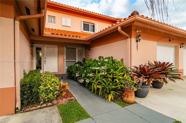 doorway to property featuring a garage, a tile roof, and stucco siding