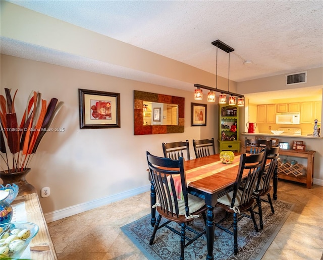 dining area with a textured ceiling, visible vents, and baseboards