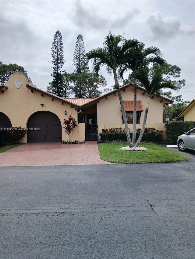 view of front of home featuring an attached garage, a tile roof, decorative driveway, and stucco siding