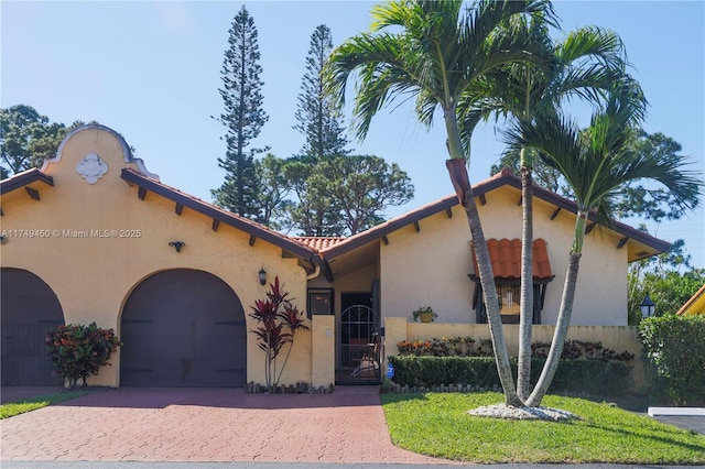 view of front facade featuring a tiled roof, stucco siding, decorative driveway, an attached garage, and a gate