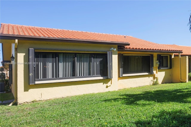 back of property with stucco siding, a tiled roof, and a yard