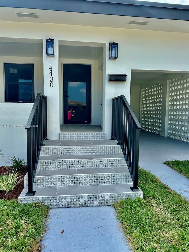 entrance to property featuring visible vents and stucco siding