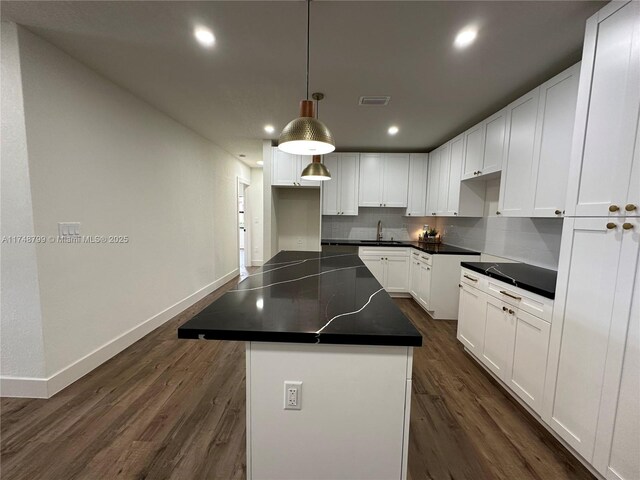 kitchen with pendant lighting, dark countertops, white cabinetry, a kitchen island, and a sink