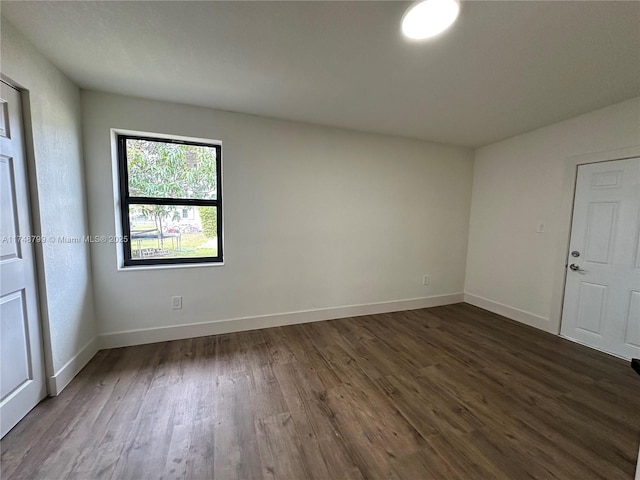 spare room featuring dark wood-style floors and baseboards