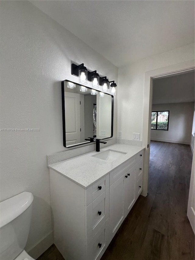 bathroom with toilet, baseboards, wood finished floors, and vanity