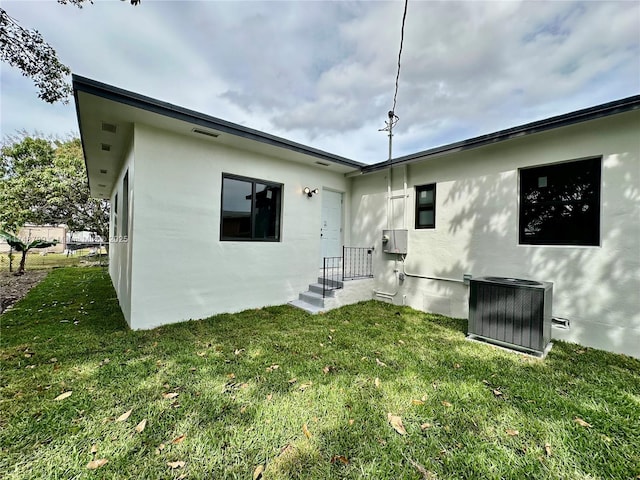 rear view of house with stucco siding, a yard, and central air condition unit