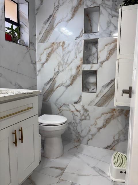 bathroom with toilet, stone wall, and vanity