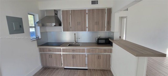 kitchen with a sink, visible vents, wall chimney range hood, electric panel, and black appliances