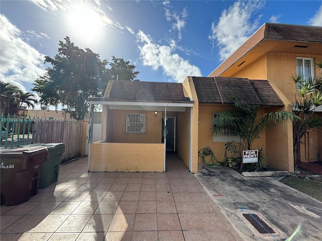 view of front facade featuring a shingled roof, fence, and stucco siding