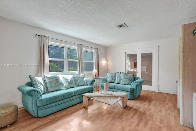 living room featuring french doors, visible vents, light wood-style flooring, and a textured ceiling