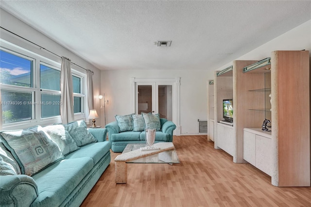 living room with a textured ceiling, light wood finished floors, and visible vents