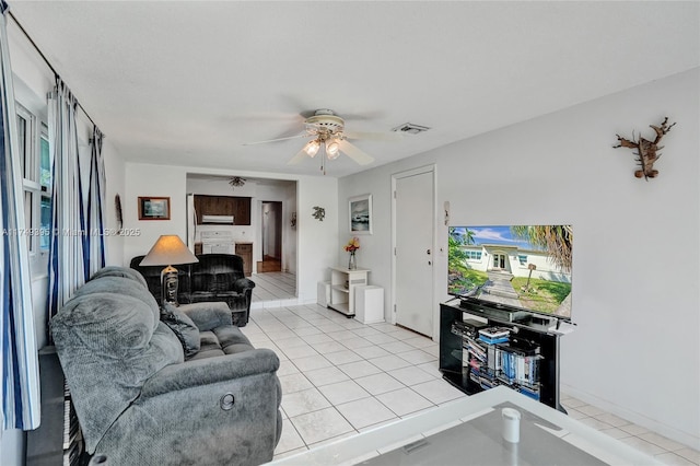 living room featuring light tile patterned floors, ceiling fan, visible vents, and baseboards