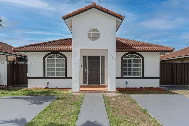 view of front of home with a tile roof, fence, a front lawn, and stucco siding