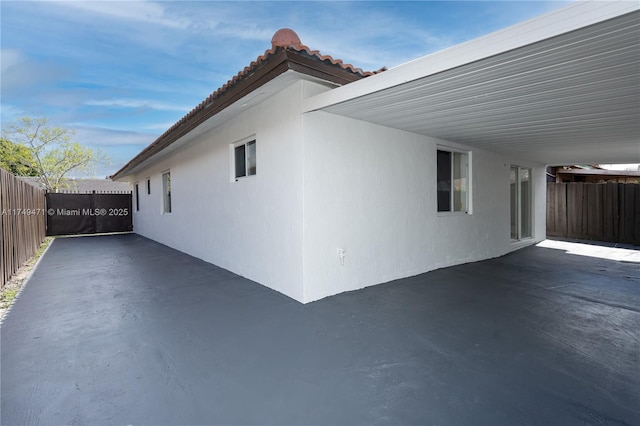 view of side of home featuring a patio, an attached carport, fence, and stucco siding