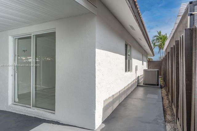 view of side of home with central AC unit, fence, and stucco siding