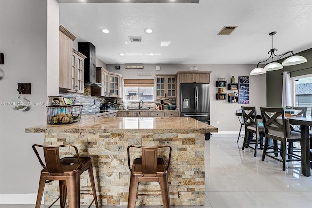 kitchen featuring glass insert cabinets, a breakfast bar, a peninsula, light countertops, and stainless steel refrigerator with ice dispenser