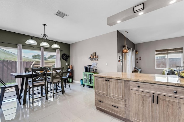 kitchen featuring light tile patterned floors, visible vents, light stone countertops, light brown cabinetry, and decorative light fixtures