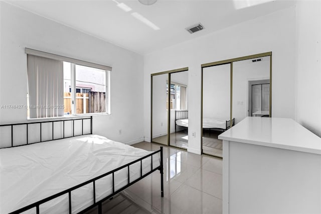 bedroom featuring light tile patterned floors, visible vents, and two closets