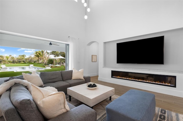 living area with baseboards, arched walkways, a glass covered fireplace, wood finished floors, and a high ceiling