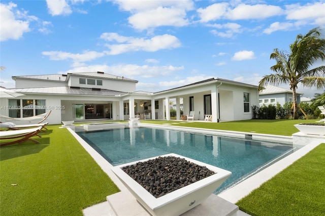 rear view of house featuring a lawn, a standing seam roof, a patio area, metal roof, and an outdoor pool