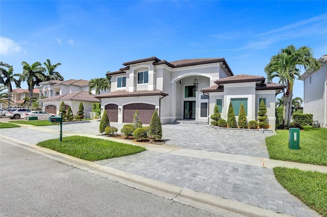 mediterranean / spanish-style house with a garage, a tile roof, decorative driveway, a residential view, and stucco siding