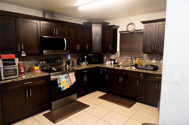 kitchen featuring dark brown cabinetry, a sink, appliances with stainless steel finishes, light stone countertops, and tasteful backsplash