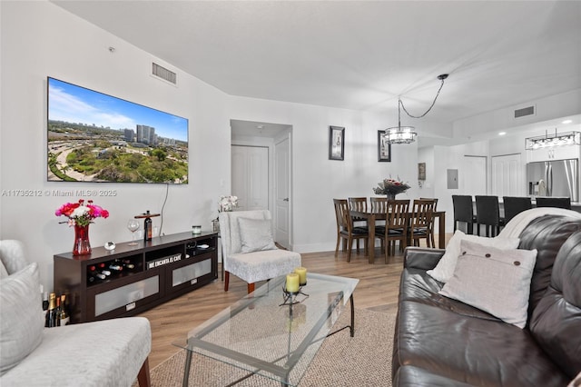 living area with an inviting chandelier, light wood-style flooring, visible vents, and baseboards