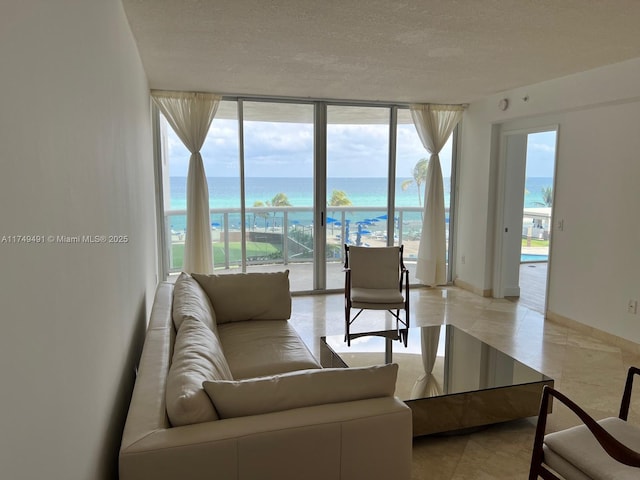 living area featuring a beach view, a water view, a textured ceiling, a wall of windows, and baseboards