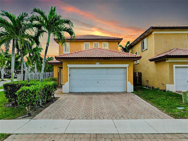 mediterranean / spanish house featuring an attached garage, fence, decorative driveway, and stucco siding