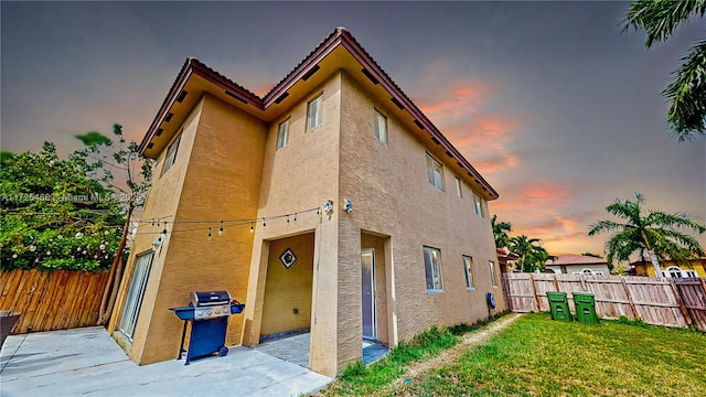 back of property at dusk featuring a lawn, a patio area, fence private yard, and stucco siding