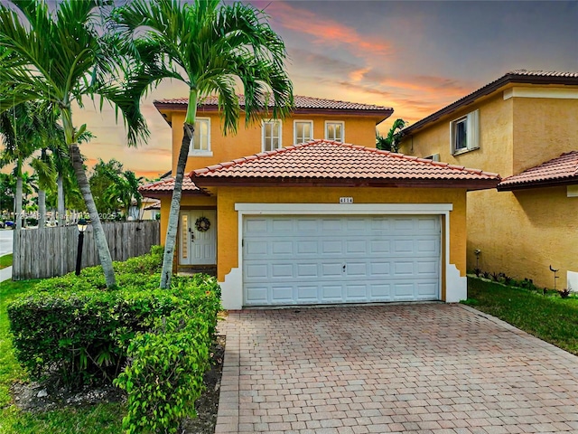 mediterranean / spanish-style house featuring a garage, decorative driveway, fence, and stucco siding