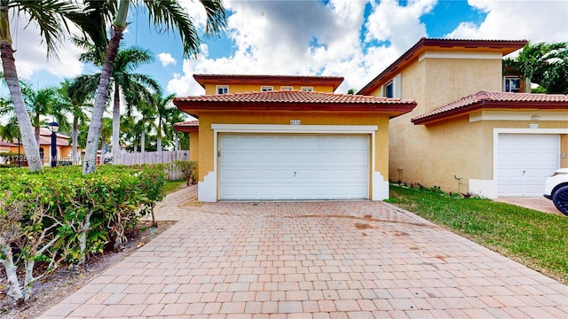 mediterranean / spanish-style house featuring decorative driveway, an attached garage, fence, and stucco siding