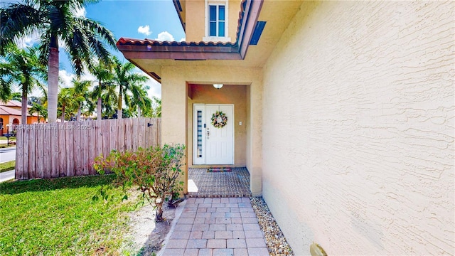 doorway to property with a tiled roof, fence, and stucco siding