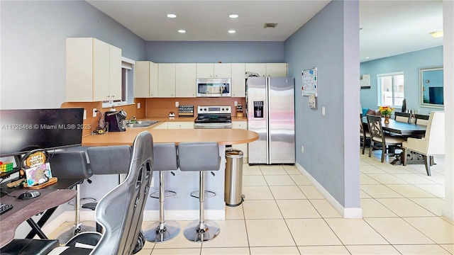 kitchen with light tile patterned floors, stainless steel appliances, a peninsula, a kitchen breakfast bar, and light countertops