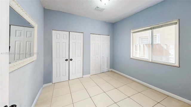 unfurnished bedroom featuring multiple closets, visible vents, light tile patterned flooring, a textured ceiling, and baseboards