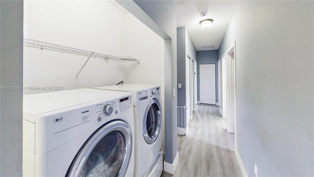 washroom with a textured ceiling, laundry area, baseboards, light wood finished floors, and washing machine and clothes dryer